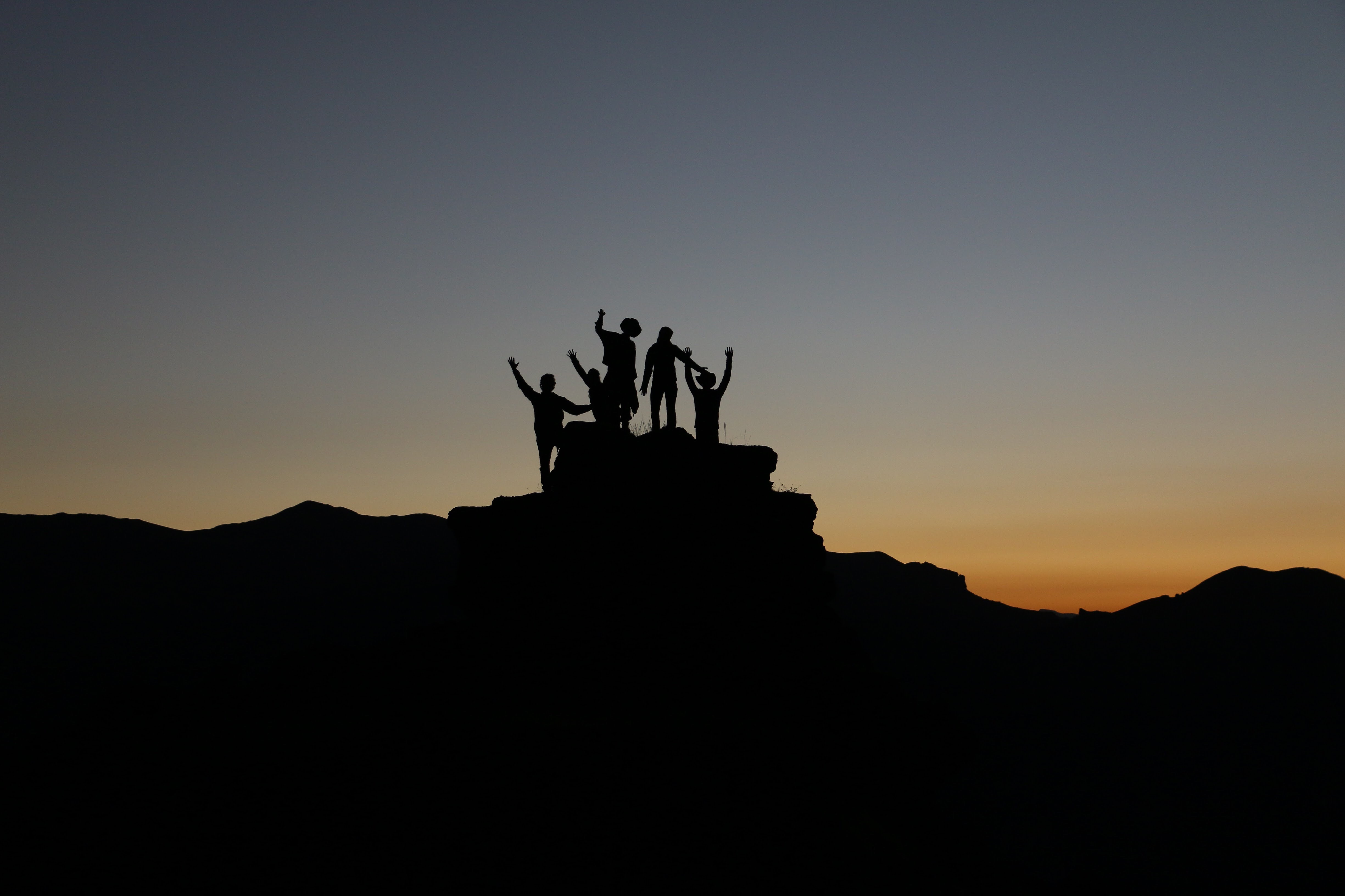 Figures in silhouette raising their hands on top of a mountain at sunset